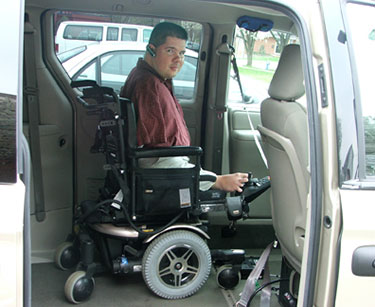A young man who does not have arms, in a wheelchair, inside a minivan.